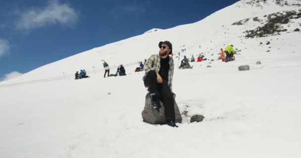 Rússia, Cáucaso. Um homem senta-se numa pedra numa montanha coberta de neve — Vídeo de Stock