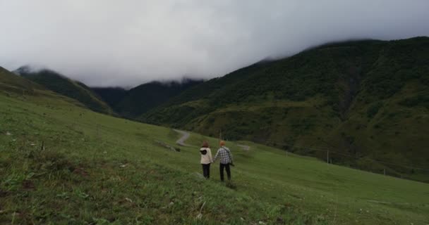 Rusia, Cáucaso. Una joven pareja está caminando por el lado herboso de la montaña — Vídeos de Stock