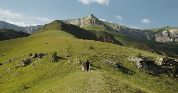 Росія, Кавказ. Молода пара спускається з пагорба, тримаючись за руки. — стокове відео