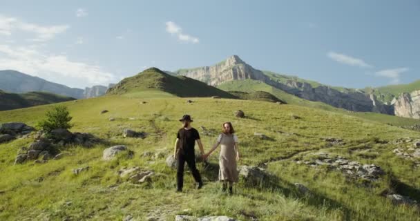 Rusland, Kaukasus. Een jong koppel daalt af van een heuvel hand in hand — Stockvideo