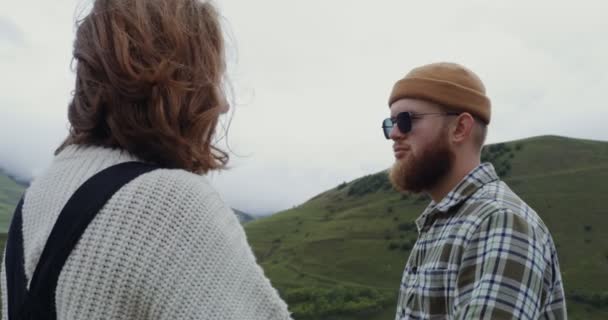 Молодая пара смотрит друг на друга улыбаясь, стоя напротив гор — стоковое видео