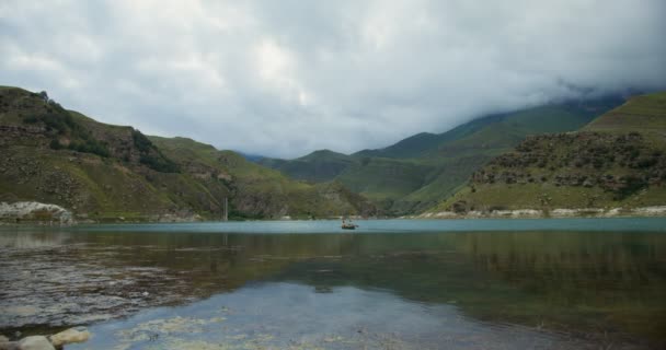 Una joven pareja está navegando en bote de remos, a través del lago contra el telón de fondo de las montañas — Vídeo de stock