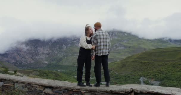 Ein junges Paar steht auf der Brüstung und umarmt sich vor der Bergkulisse — Stockvideo