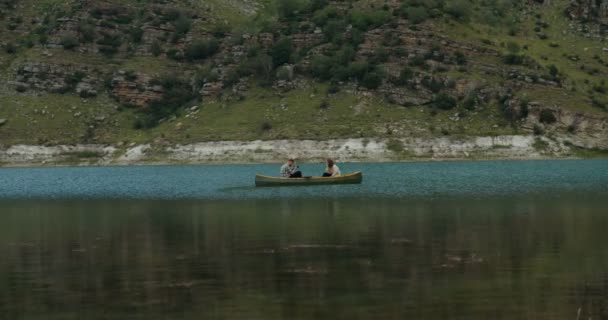 En kille fotograferar en tjej som sitter i en roddbåt i fjällsjön. — Stockvideo