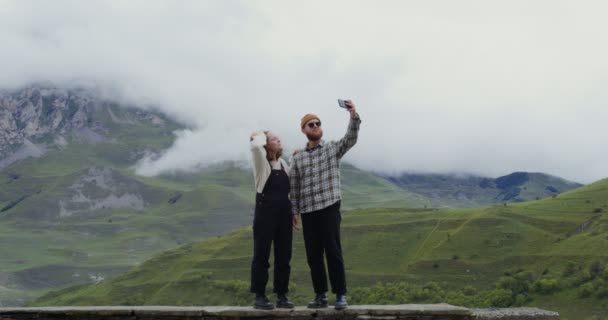 Ett ungt par tar selfie på mobilen, står mot bakgrund av berg — Stockvideo