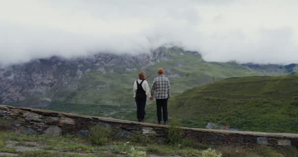 Una joven pareja se para en el parapeto abrazándose contra el telón de fondo de las montañas — Vídeos de Stock