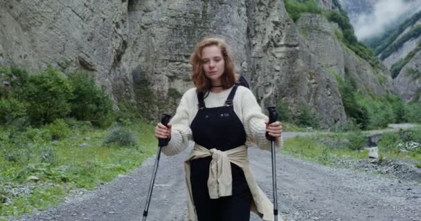 Эльбрус. Молодая женщина стоит на горной дороге с палками для спортивной ходьбы — стоковое видео