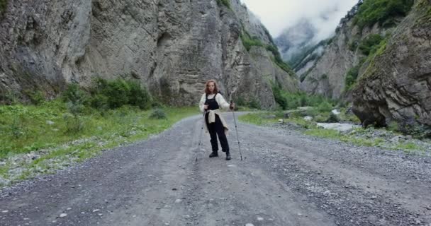 Elbrus. ung kvinna står på bergsvägen med pinnar för sport promenader — Stockvideo