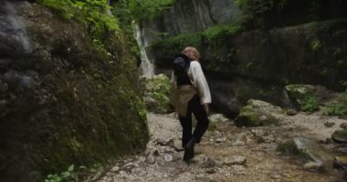 Rusya, Kafkasya. Genç bir kadın taşların üzerinde kaynayan bir dağ deresini geçiyor.