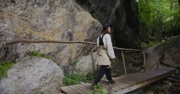 Russland, Kaukasus. Eine Frau überquert einen schnellen Gebirgsfluss auf einer Holzbrücke — Stockvideo