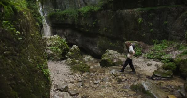 Rosja, Kaukaz. Młoda kobieta przechodzi przez strumień górski na kamieniach. — Wideo stockowe