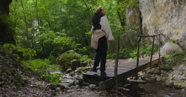 Russia, Caucaso. Una donna attraversa un fiume di montagna veloce su un ponte di tronchi — Video Stock