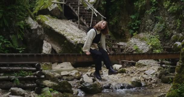 Ryssland, Kaukasus. En ung kvinna sitter på ribban över en sjudande bergsflod. — Stockvideo