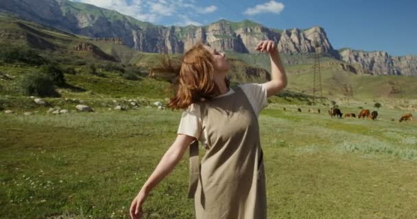 The Caucasus. A young woman dances relaxedly on cows pasture between mountains — Stock Video