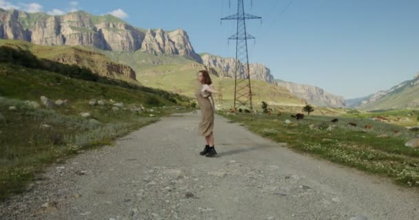 De Kaukasus. Een jonge vrouw danst op de weg in de buurt van koeien weiland tussen bergen — Stockvideo
