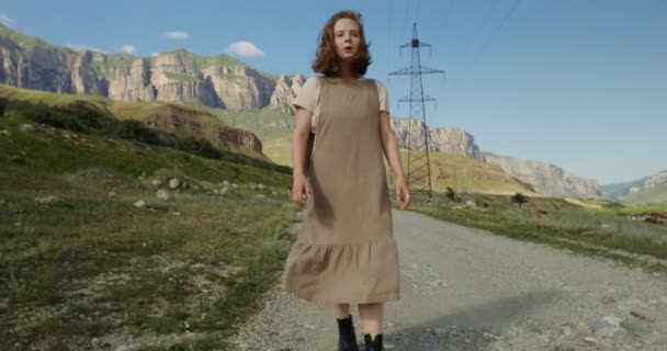 若い女性が牛の放牧地を通り、山の間を歩く — ストック動画