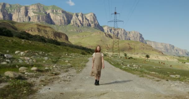 Il Caucaso.Giovane donna cammina lungo la strada passato pascolo mucche, tra le montagne — Video Stock