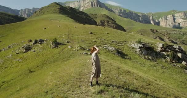 Una donna raddrizza i capelli e vestiti in piedi sulle colline di fronte alle montagne — Video Stock