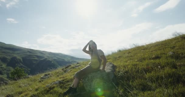 Oroszország, Kaukázus. Egy fiatal nő ül egy sziklán egy domb lejtőjén. — Stock videók