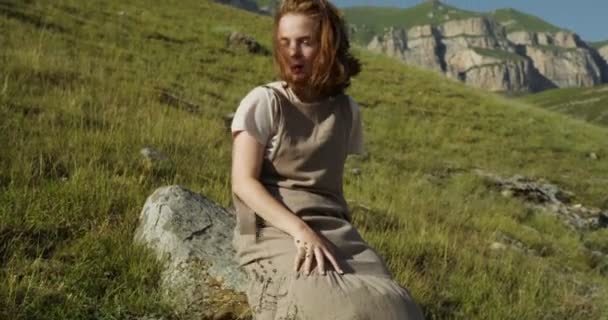 ロシア、コーカサス。若い女性が丘の斜面に石の上に座っている — ストック動画
