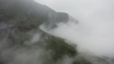 Yoğun bulutlarla kaplı yüksek dağ yamaçlarının hava fotoğrafları.