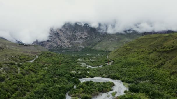 Dağlık bir vadi, ovalarda nehir ve bulutlarla kaplı kayalık dağlar. — Stok video