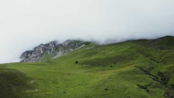 Холмистая местность, с травой с скалистыми горами, вершины покрыты облаками — стоковое видео