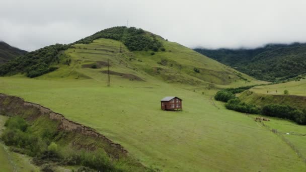 Самотній дерев'яний будинок на палях у полі в гірській долині серед зелених пагорбів — стокове відео