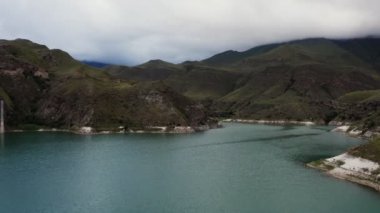 Yeşil tepeler arasında düzensiz şekilli berrak dağ gölü manzarası