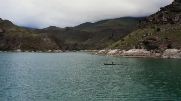 男と女が岩の多い山の間の湖の上のボートに乗って航海している — ストック動画