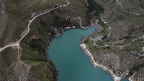 Une vue d'un lac de montagne clair de forme irrégulière situé entre des collines verdoyantes — Video