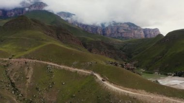 Arabalar dar çakıllı bir dağ yolu boyunca dik bir çim yamacına doğru sürüyorlar.