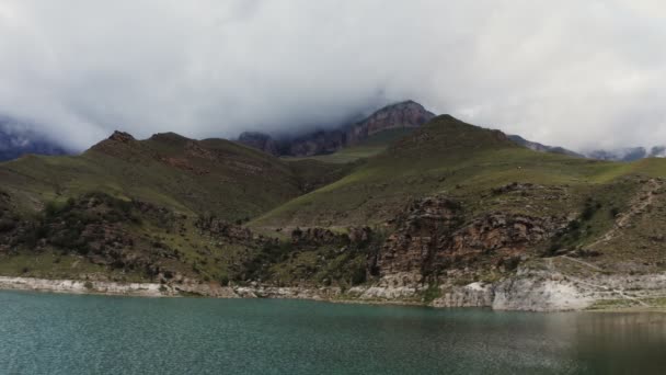 Un lac de montagne au pied des montagnes avec des pentes herbeuses et des falaises rocheuses — Video