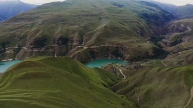 Yeşil tepeler arasında düzensiz şekilli berrak dağ gölü manzarası