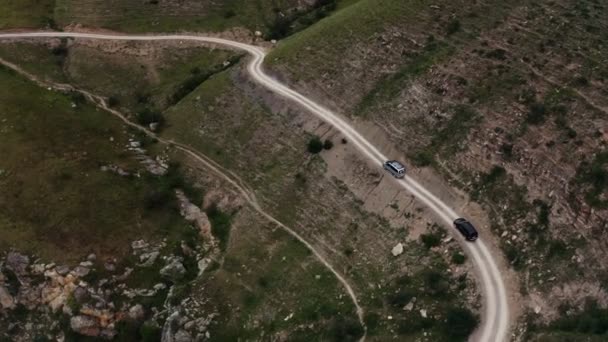 Samochody jadą wąską, żwirową górską drogą na strome trawiaste zbocze — Wideo stockowe