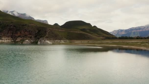 Гірська долина, озеро серед трав'янистих пагорбів біля підніжжя скелястих гір — стокове відео