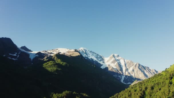 El pico nevado de Elbrus entre montañas cubiertas de bosques verdes — Vídeos de Stock