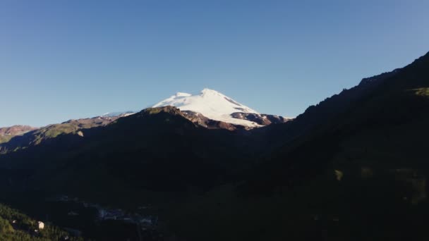 Ośnieżony szczyt Elbrus wznosi się nad górską doliną w promieniach słońca — Wideo stockowe
