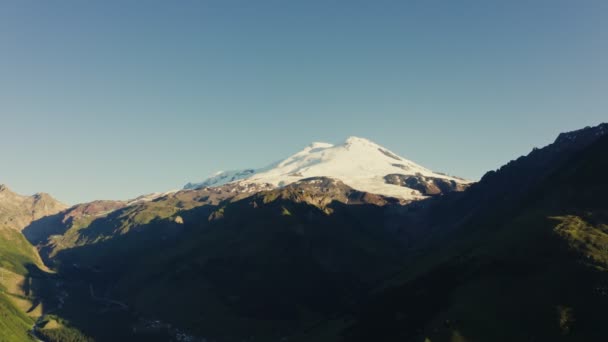 Snow-capped peak of Elbrus rises above mountain valley in rays of the sun — Stock Video