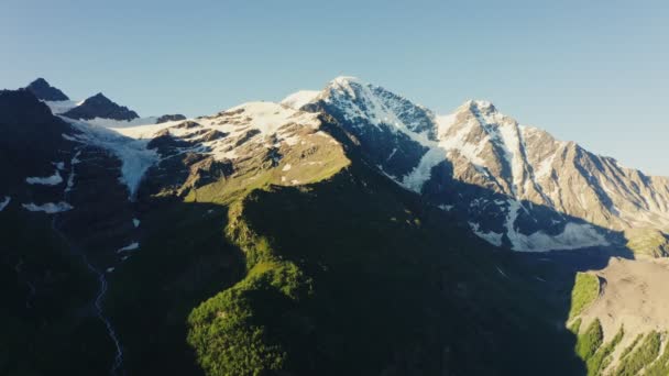 Un bosque verde en las laderas de las montañas da paso a la nieve en las cimas — Vídeos de Stock