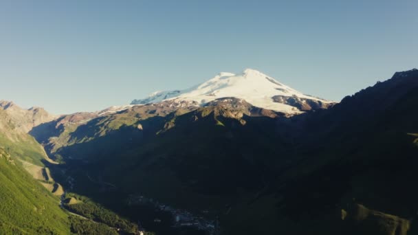Χιονισμένη κορυφή του Έλμπρους υψώνεται πάνω από την κοιλάδα του βουνού σε ακτίνες του ήλιου — Αρχείο Βίντεο