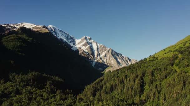 Ośnieżony szczyt Elbrus wznosi się nad górską doliną w promieniach słońca — Wideo stockowe