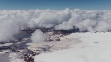 Karla kaplı bir dağ zirvesinden kümülüs bulutlarıyla kaplı bir vadiye bir manzara.