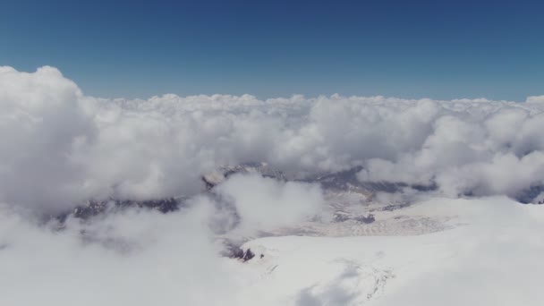 Blick von einem schneebedeckten Berggipfel auf ein Tal mit Kumuluswolken — Stockvideo