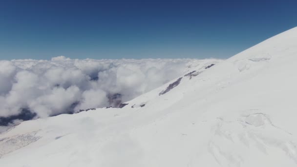 Uma vista de um pico de montanha coberto de neve para um vale coberto com nuvens cumulus — Vídeo de Stock