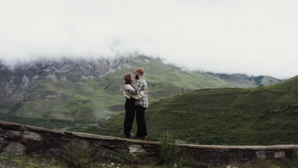 Una giovane coppia si erge sul parapetto abbracciandosi sullo sfondo delle montagne — Video Stock