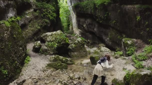Μια νεαρή γυναίκα περπατά πάνω από τις πέτρες κατά μήκος του ποταμού του βουνού που βράζει — Αρχείο Βίντεο