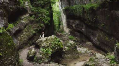 Genç bir kadın bir dağ geçidinde taşların arasında yürüyor.