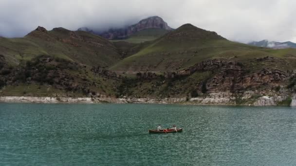 한 남녀가 바위투성이 의산들 사이에 있는 호수에서 노젓는 배를 타고 가고 있다 — 비디오