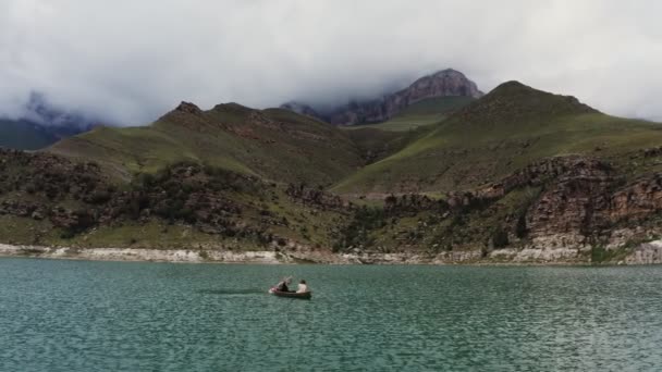 Un homme et une femme naviguent sur une barque sur un lac au milieu des montagnes rocheuses — Video